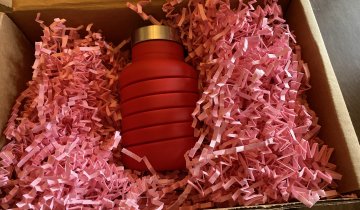 red que Bottle nestled in brown box full of pink raffia