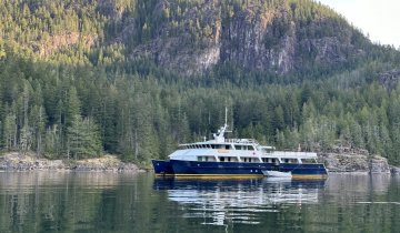 The Cascadia anchored in front of a forested island.